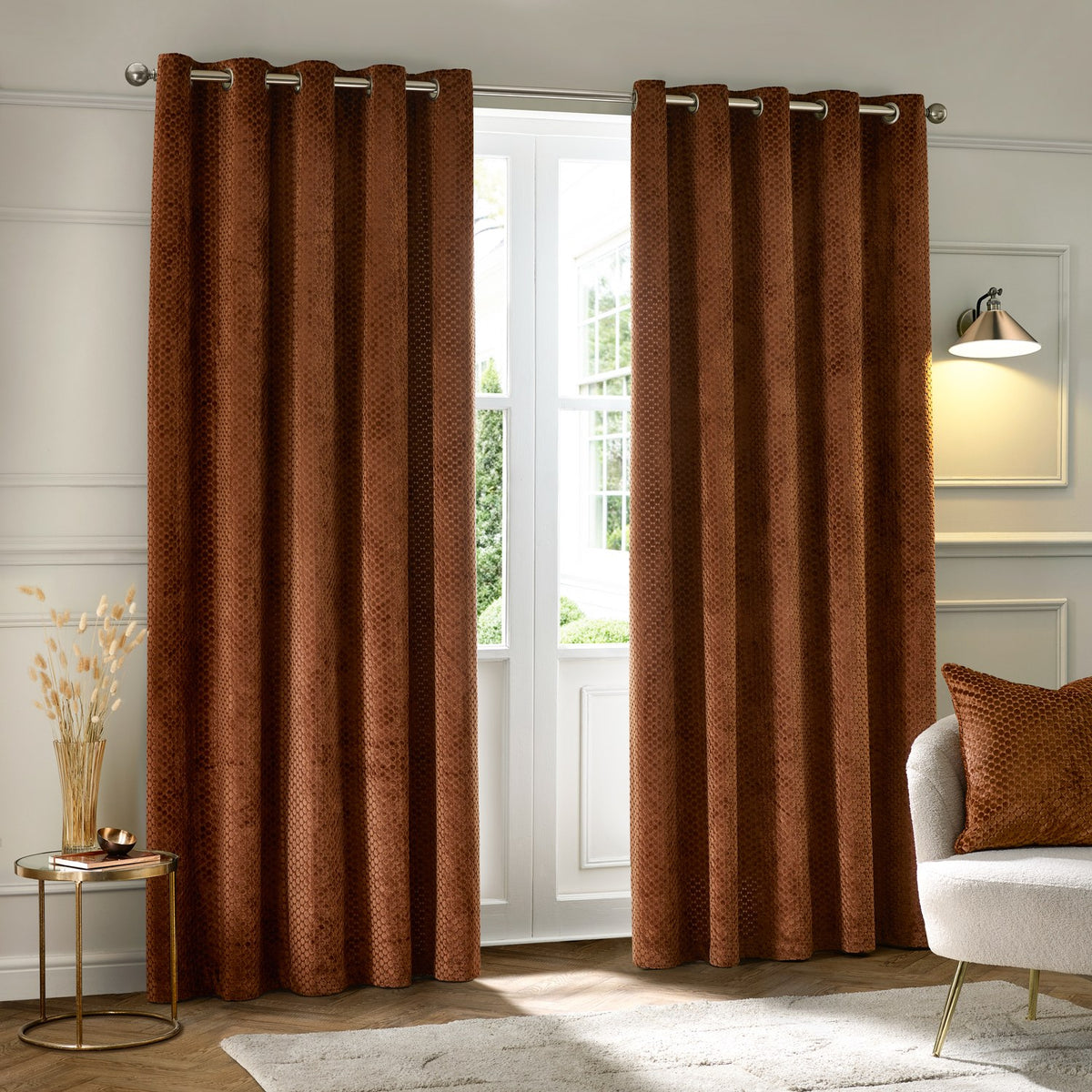 Neptune Velvet Fully Lined Eyelet Curtains in copper, hung floor-length with honeycomb-textured velvet fabric, shown framing a bright living room window.