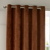 Neptune Velvet Fully Lined Eyelet Curtains in copper, showing honeycomb-textured velvet fabric on silver eyelet rings and pole, hung beside a window.