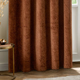 Neptune Velvet Fully Lined Eyelet Curtains in copper, showing the honeycomb-textured fabric in soft folds, styled in a living room beside a round brass side table.