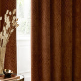 Neptune Velvet Fully Lined Eyelet Curtains in copper, showing honeycomb-textured fabric folds by a window, styled in a living room with dried grasses and a round side table.