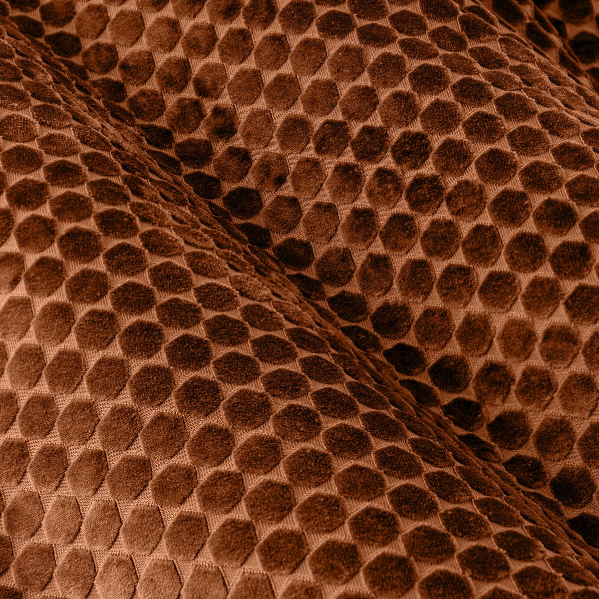 Close-up of Neptune Velvet Eyelet Curtains in copper, showing a raised honeycomb pattern in the polyester velvet fabric with soft folds catching the light.