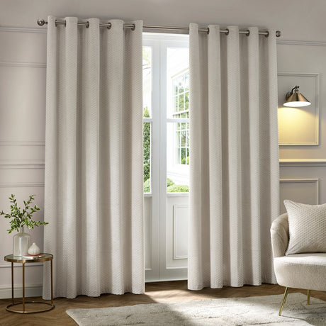 Neptune Velvet Fully Lined Eyelet Curtains in ivory with textured honeycomb pile, shown as a full-length pair on a metal rail in a living room setting.