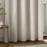Neptune Velvet Fully Lined Eyelet Curtains in ivory, showing a honeycomb dot cut-pile texture, styled in a living room beside a round side table and potted plant.