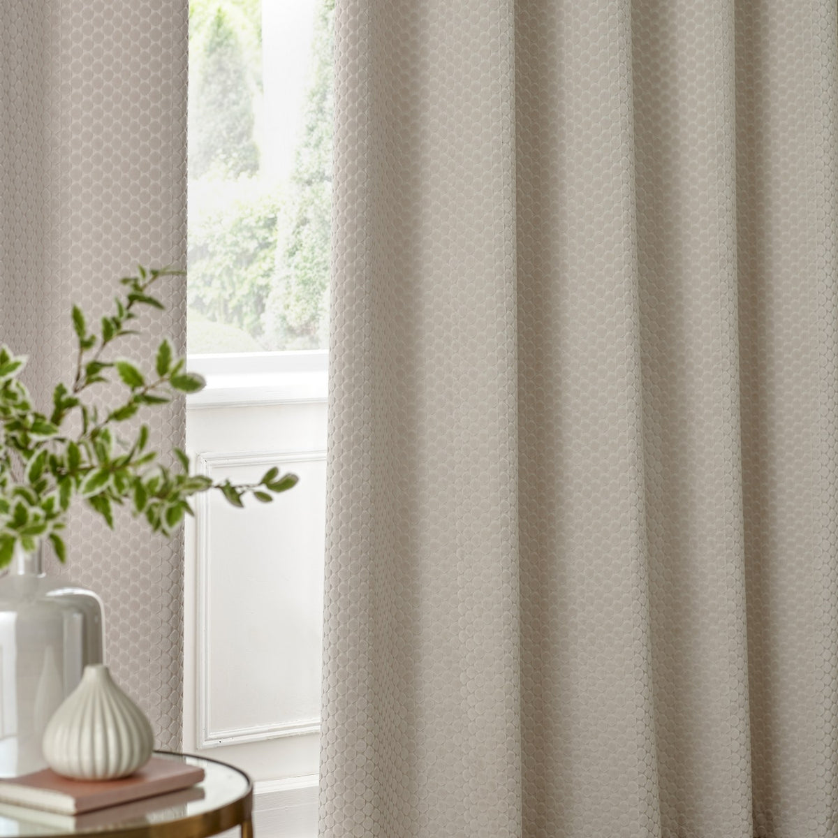 Neptune Velvet Fully Lined Eyelet Curtains in ivory, shown hanging in a living room window with a honeycomb-textured pile and soft folds.