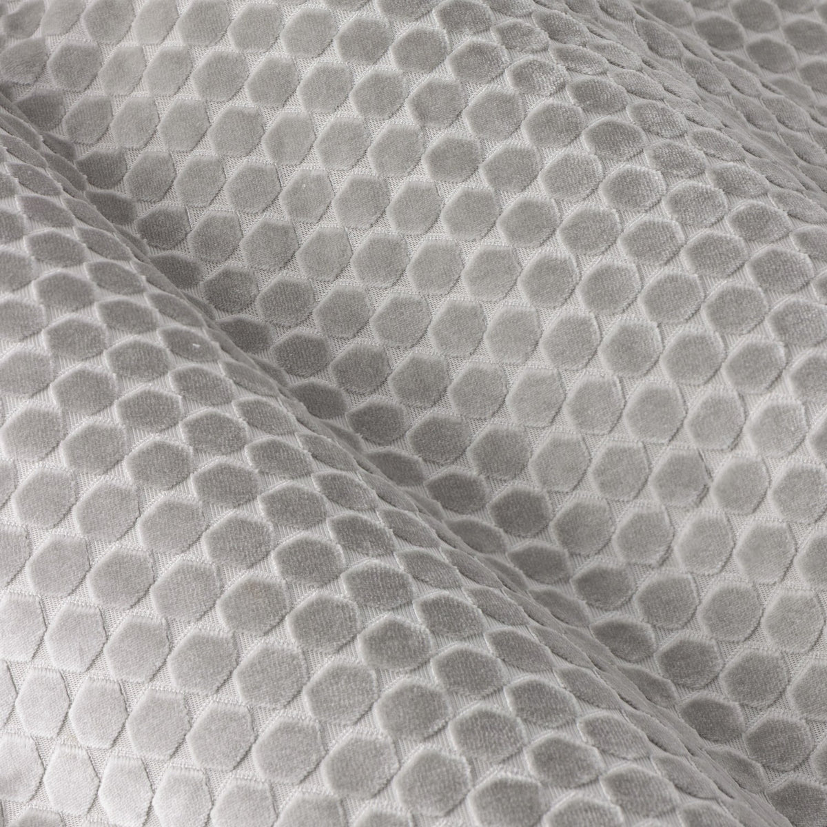 Close-up of Neptune silver grey cut velvet eyelet curtain fabric, showing a raised geometric dot pattern with light-catching pile texture and soft folds.