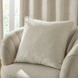 Neptune Geometric Velvet Cushion in ivory with a raised honeycomb-style pattern, shown on a boucle armchair beside a curtained window.