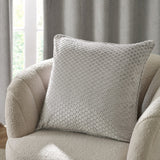 Neptune Geometric Velvet Cushion in silver grey with raised honeycomb dot texture, shown on a cream boucle armchair against curtains.