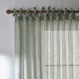Nimbus sheer tie-top curtain panel in eucalyptus green polyester, fabric ties knotted over a wooden pole, showing the woven texture against a light room.