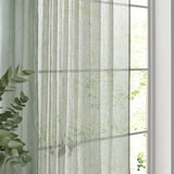 Nimbus sheer tie-top curtain panel in eucalyptus green polyester, hanging by a window with soft daylight and greenery visible through the fabric.