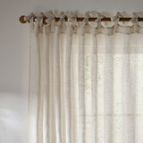 Nimbus sheer tie-top curtain panel in natural polyester, hung from a wooden pole with fabric tie knots, showing a loosely woven, light-filtering texture against a window.