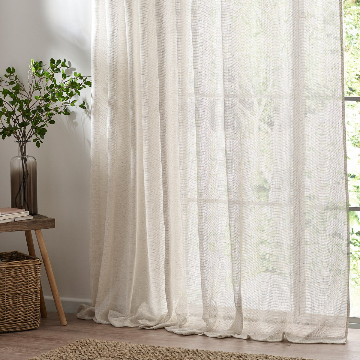 Nimbus Plain Polyester Curtain Panel in natural, sheer tie-top fabric hanging at a bright window beside a wooden side table and potted plant.