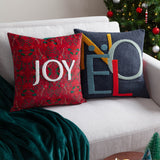 Noel Plain Polyester Cushion in charcoal-navy with tufted NOEL lettering, shown beside a red floral JOY cushion on a sofa near a Christmas tree.