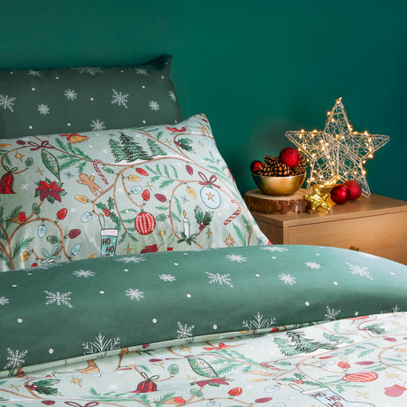 Noelle Printed Reversible Duvet Cover Set in green, styled on a bed with festive Christmas motifs on one side and snowflake-print green reverse, shown in a bedroom setting.