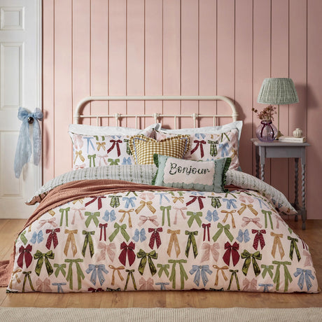 Noortje Silk Abstract Duvet Cover Set in Silk Pink, featuring a bow print in green, blue, gold and red on a pink bed with matching pillows in a pink-panelled bedroom.