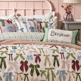 Noortje Silk Abstract Duvet Cover Set in pink polycotton, printed with bows in green, blue, red and gold, styled on a bed with a "Bonjour" cushion in a pink bedroom.