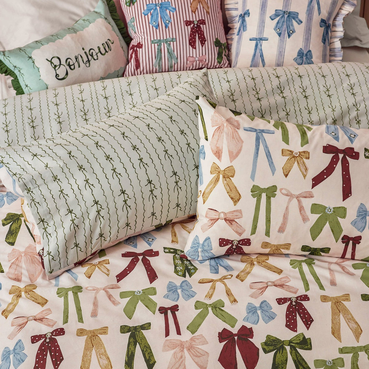 Noortje Silk Abstract Duvet Cover Set in pink with an allover bow print in green, blue, gold and red, shown with matching pillowcases and a striped leaf-pattern reverse.