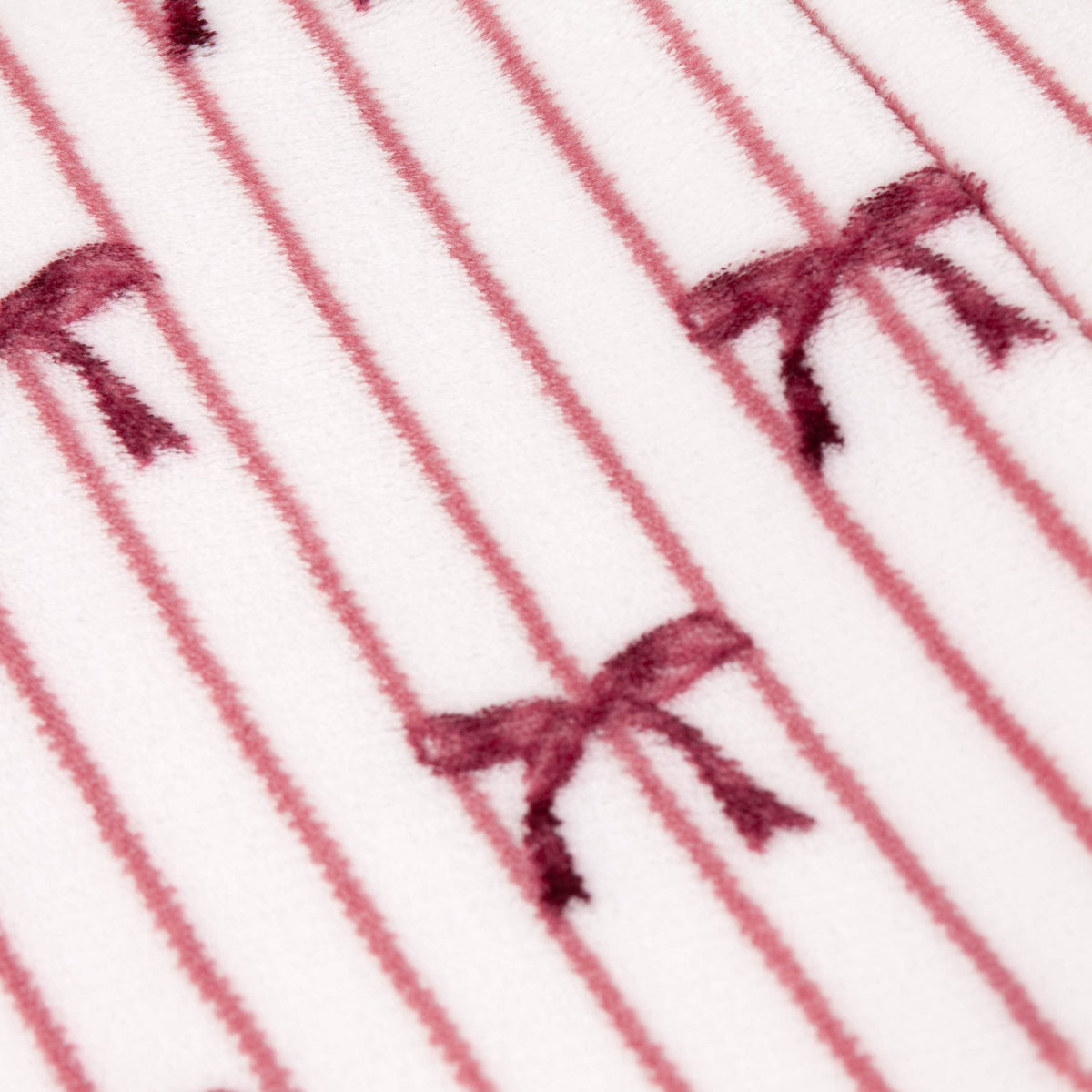 Noortje Bows Silk Throw in silk pink, close-up of fleece fabric with thin vertical stripes and scattered bow motifs in deep rose-red on a white ground.