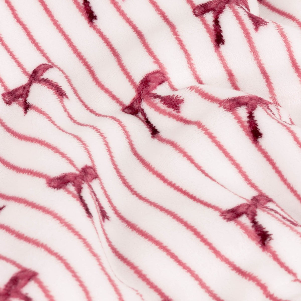 Noortje Bows Silk Throw in pink, close-up of the fleece fabric showing thin rose-red vertical stripes and small bow motifs on a white ground, softly draped.