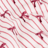 Noortje Bows Silk Throw in pink, close-up of the fleece fabric showing thin rose-red vertical stripes and small bow motifs on a white ground, softly draped.