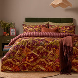 Nya Woodland Reversible Striped Duvet Cover Set in burgundy, styled on a bed with woodland animal print, striped reverse edging, and matching pillowcases in a bedroom setting.