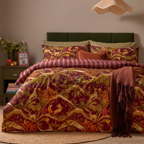 Nya Woodland Reversible Striped Duvet Cover Set in burgundy, styled on a bed with woodland animal print, striped reverse edging, and matching pillowcases in a bedroom setting.