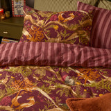Nya Woodland Reversible Striped Duvet Cover Set in burgundy on a bed, showing the woodland animal print side and reverse pink and plum striped fabric with matching pillowcase.