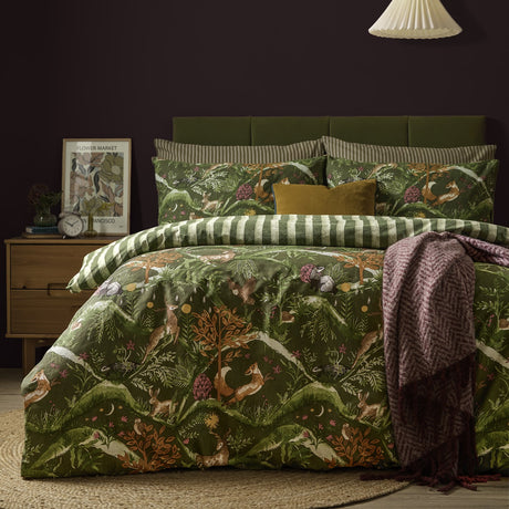 Nya Woodland Reversible Striped Duvet Cover Set in Forest green, showing a woodland animal print with foxes, hares and deer, styled on a bed with striped pillowcases in a dark bedroom.