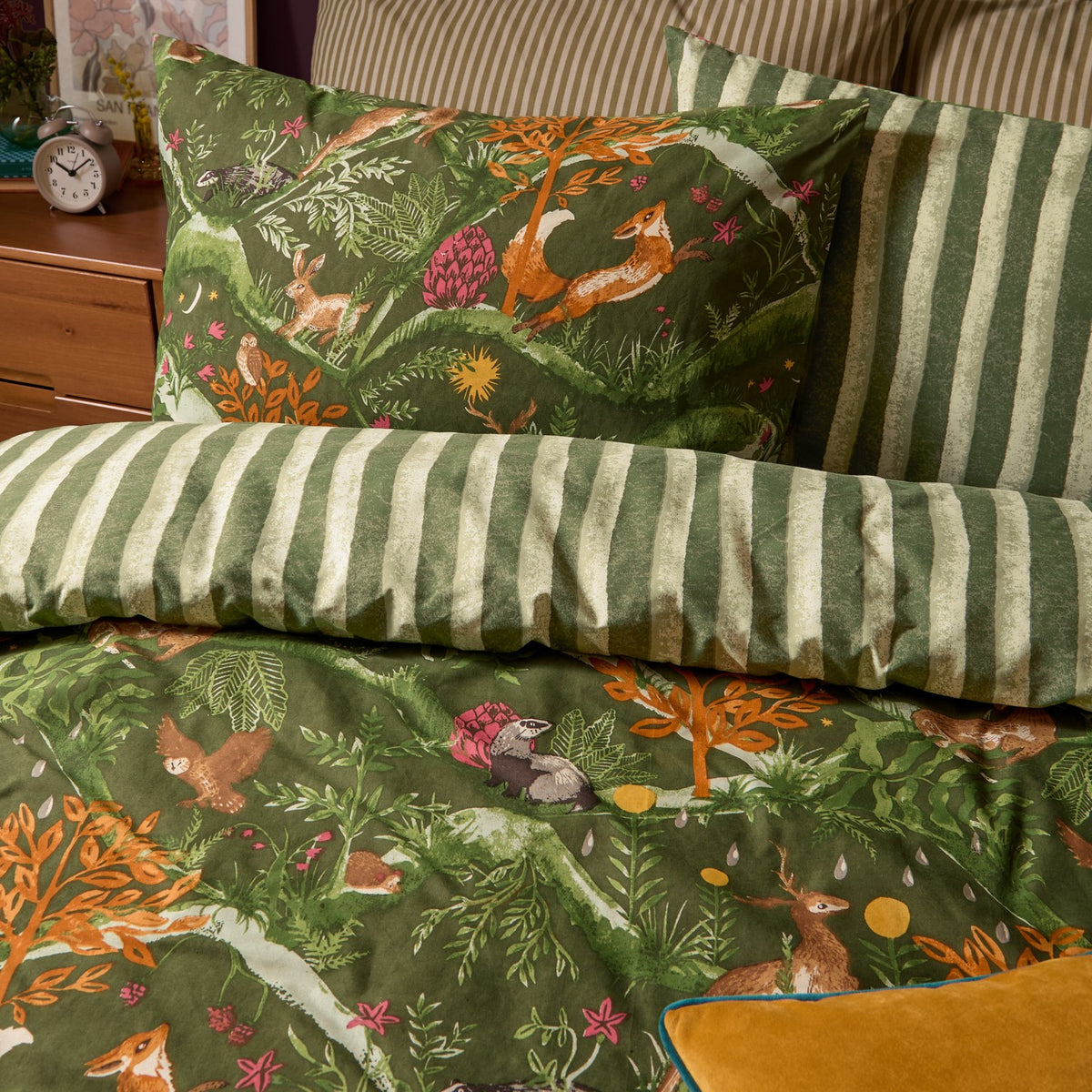 Nya Woodland Reversible Striped Duvet Cover Set in Forest, showing the woodland fox and hare print pillowcase paired with the reverse green striped side on a bedroom bed.