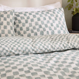 Nyhavn Reversible Check Duvet Cover Set in Aqua on a bed, showing a hand-printed brushed checkerboard pattern in aqua and white on pillowcases and duvet.