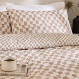 Nyhavn Reversible Check Duvet Cover Set in Tobacco, shown on a bed with matching pillowcases in a tan and off-white checkerboard pattern, styled in a bedroom with a coffee mug on a tray.