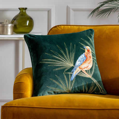 Odisha Exotic Bird Animal Velvet Cushion in emerald, square with embroidered bird in rust and blue amid gold fern fronds, shown on a mustard velvet armchair.