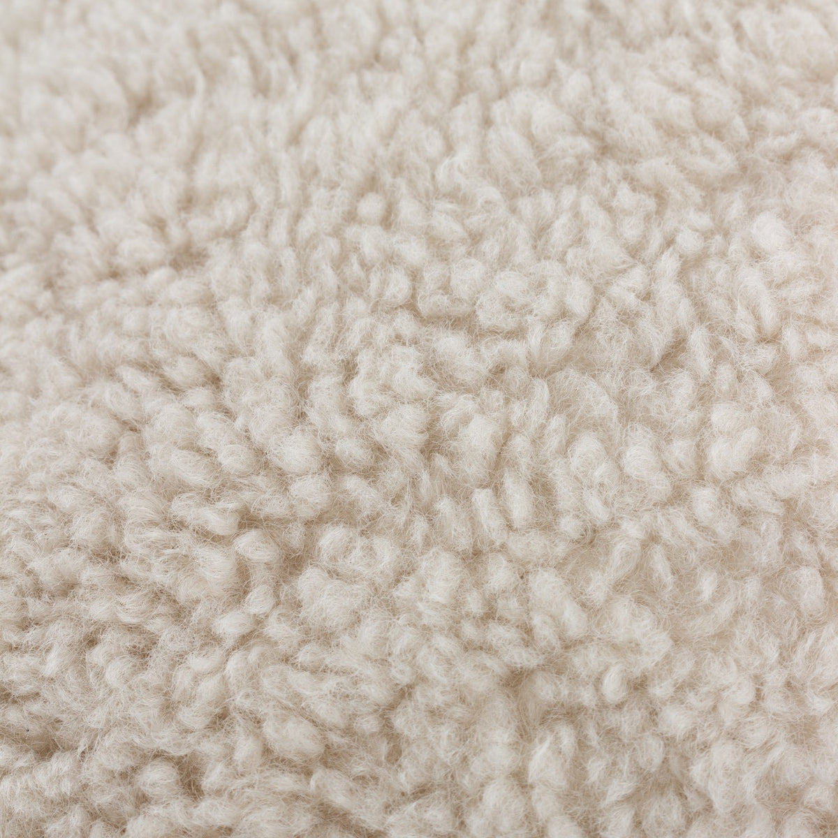 Close-up of the Olann cushion in natural beige, showing its dense, curly faux shearling pile texture on the front face.