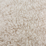 Close-up of the Olann cushion in natural beige, showing its dense, curly faux shearling pile texture on the front face.