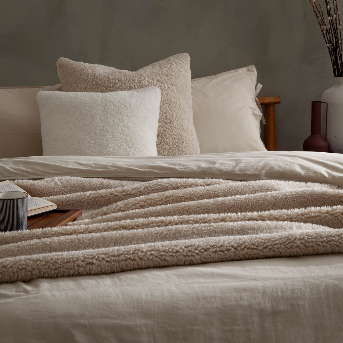 Olann Plain Velvet Throw in natural draped across a bed, showing its ribbed shearling-look faux fleece texture layered over cream bedding and cushions.