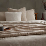 Olann Plain Velvet Throw in natural draped across a bed, showing its ribbed shearling-look faux fleece texture layered over cream bedding and cushions.