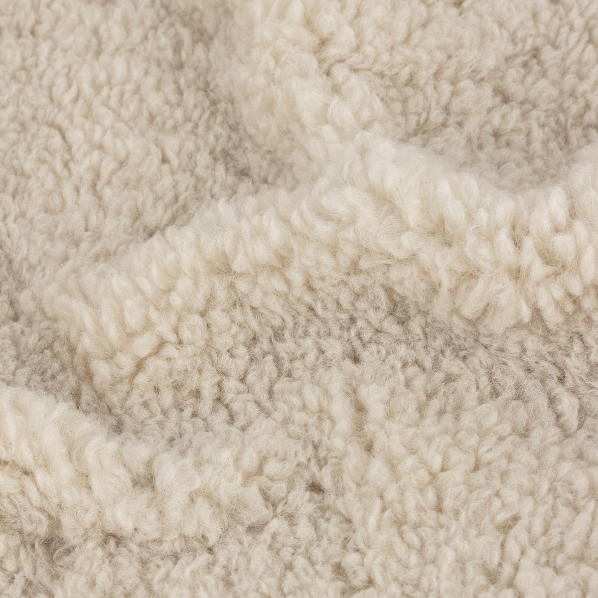 Close-up of the Olann Plain Velvet Throw in natural, showing the dense, curly shearling-look faux fleece texture on the front face.