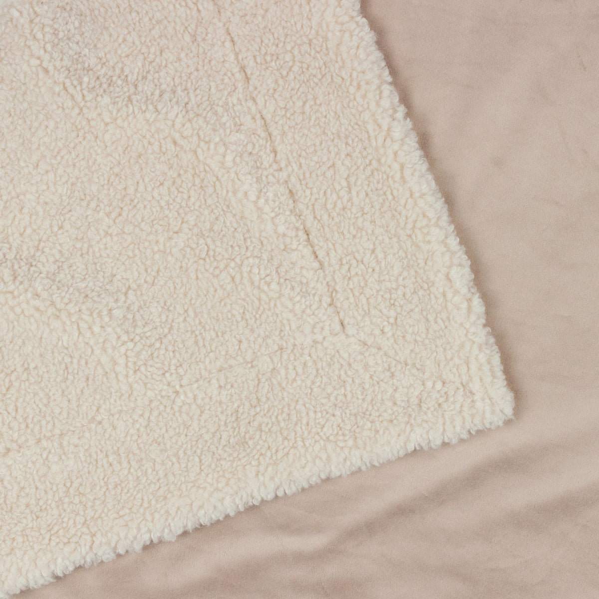 Close-up of the Olann Plain Velvet Throw in Natural, showing the dense shearling-look faux fleece front with a smooth velvet reverse against a beige background.