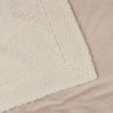 Close-up of the Olann Plain Velvet Throw in Natural, showing the dense shearling-look faux fleece front with a smooth velvet reverse against a beige background.