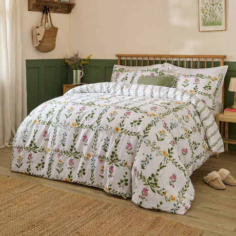 Olivia Cotton Floral Duvet Cover Set on a bed with white cotton fabric, green trellis vine print and pink, yellow and blue wildflowers, styled in a green and cream bedroom.