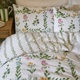 Olivia Cotton Floral Duvet Cover Set in green on a bedroom bed, white cotton fabric with pink, yellow and blue floral trellis print and green vine-stripe reverse, styled with matching pillowcases.