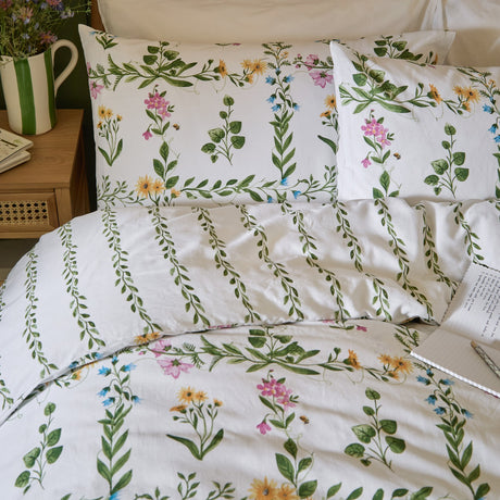 Olivia Cotton Floral Duvet Cover Set in green on a bedroom bed, white cotton fabric with pink, yellow and blue floral trellis print and green vine-stripe reverse, styled with matching pillowcases.