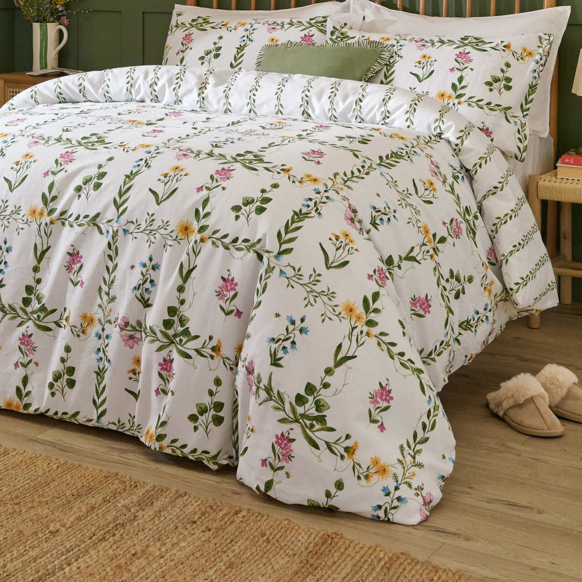 Olivia Cotton Floral Duvet Cover Set in white with a green trellis and pink, yellow and blue floral print, shown on a bed with matching pillowcases in a green-walled bedroom.