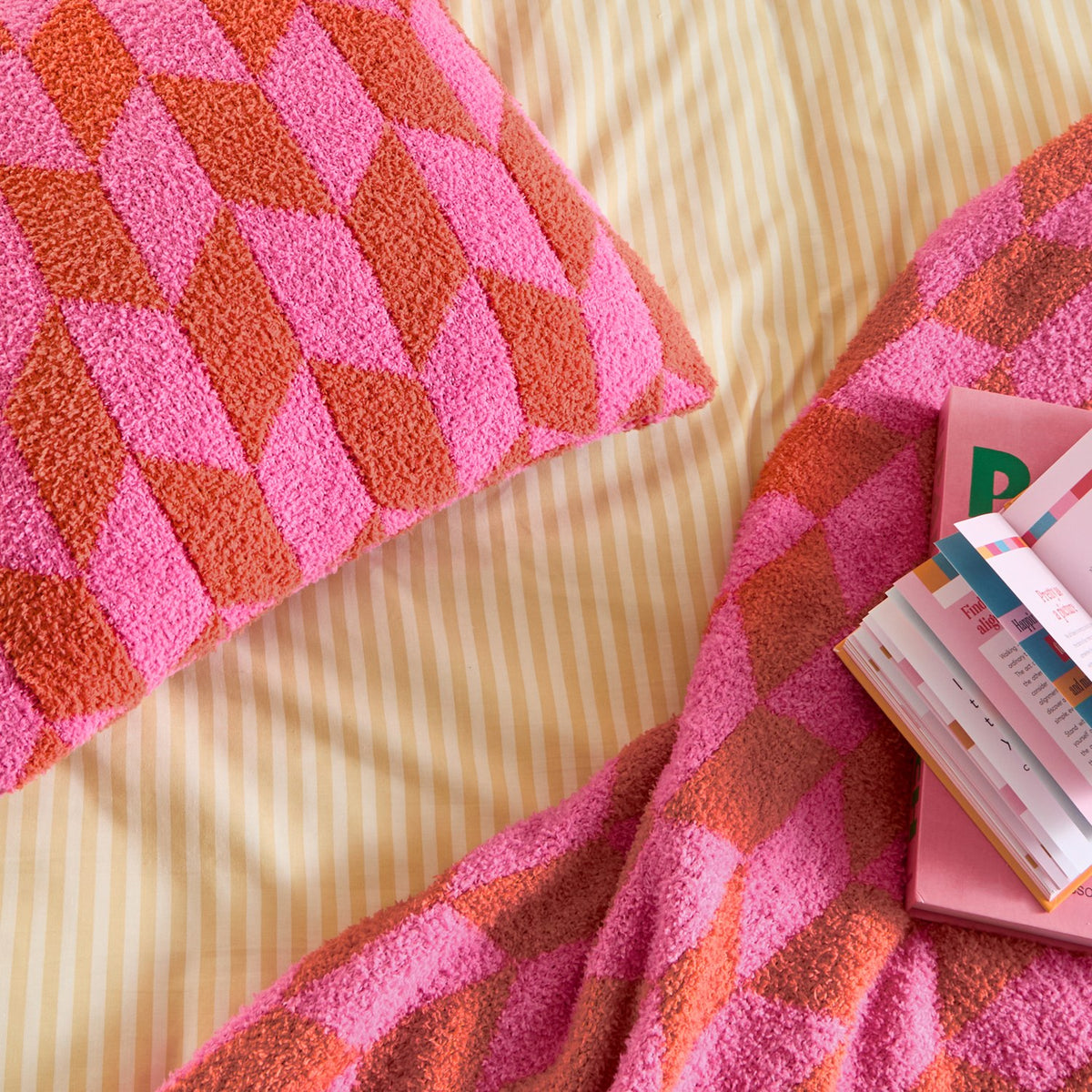 Olsen Geometric Polyester Cushion in Pink Pop, a textured square scatter cushion with an interlocking hot pink and rust geometric pattern, shown with a matching throw on striped bedding.