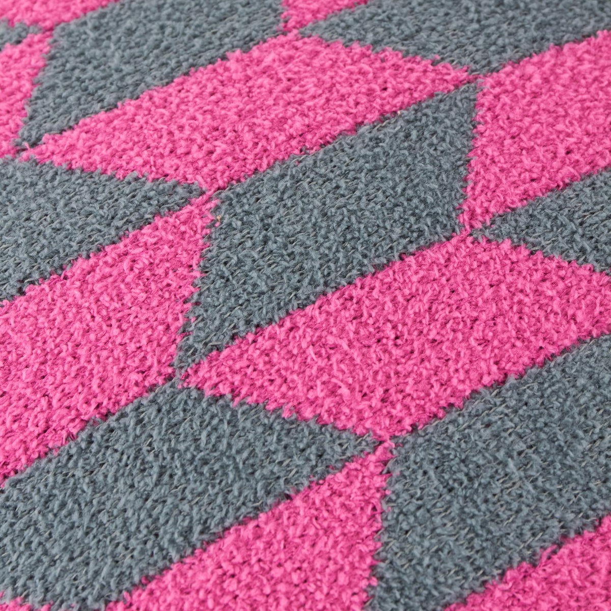 Close-up of the Olsen Geometric Polyester Cushion in Retro Pink, showing a textured knitted diamond pattern in raspberry pink and dark teal.