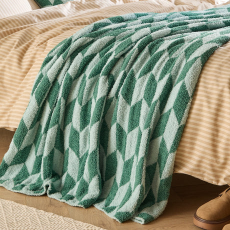 Olsen Geometric Polyester Throw in Good For You Green, a textured knitted blanket with a diamond pattern in two green tones, draped over a bed with striped bedding.