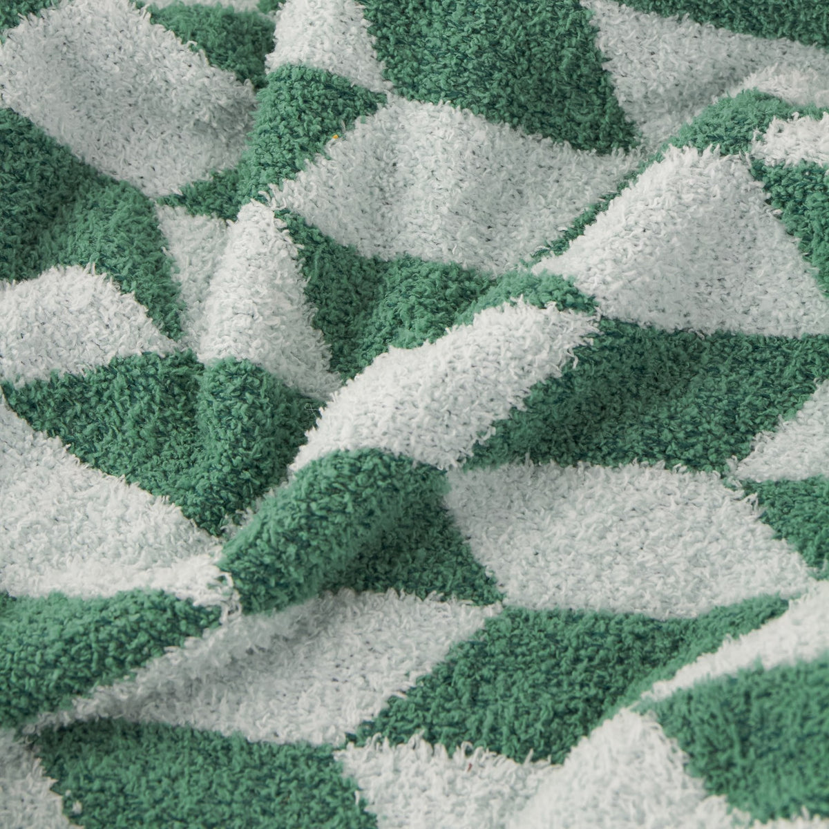 Olsen Geometric Polyester Throw in Good For You Green, close-up of the knitted feather-yarn fabric showing a bold triangular pattern in two greens against pale mint, softly draped in folds.