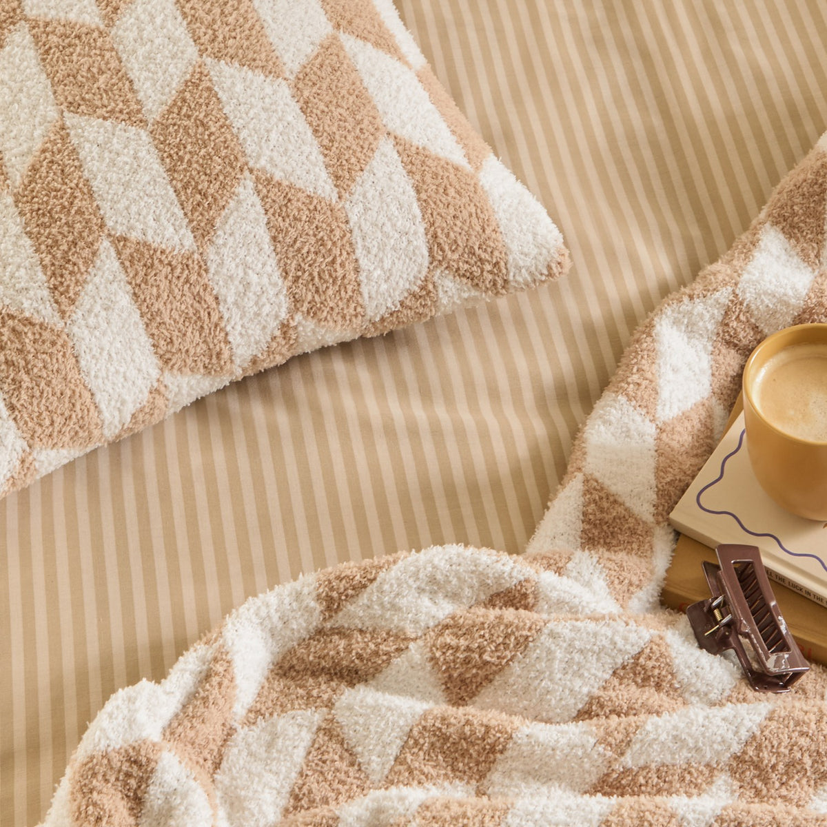 Olsen Geometric Polyester Throw in caramel and cream, knitted with a bold interlocking block pattern and brushed pile, shown draped with a matching pillow on beige striped bedding.