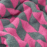 Olsen Geometric Polyester Throw in Retro Pink, close-up of the knitted textured fabric showing an angular pink and teal tessellating pattern, draped in soft folds.