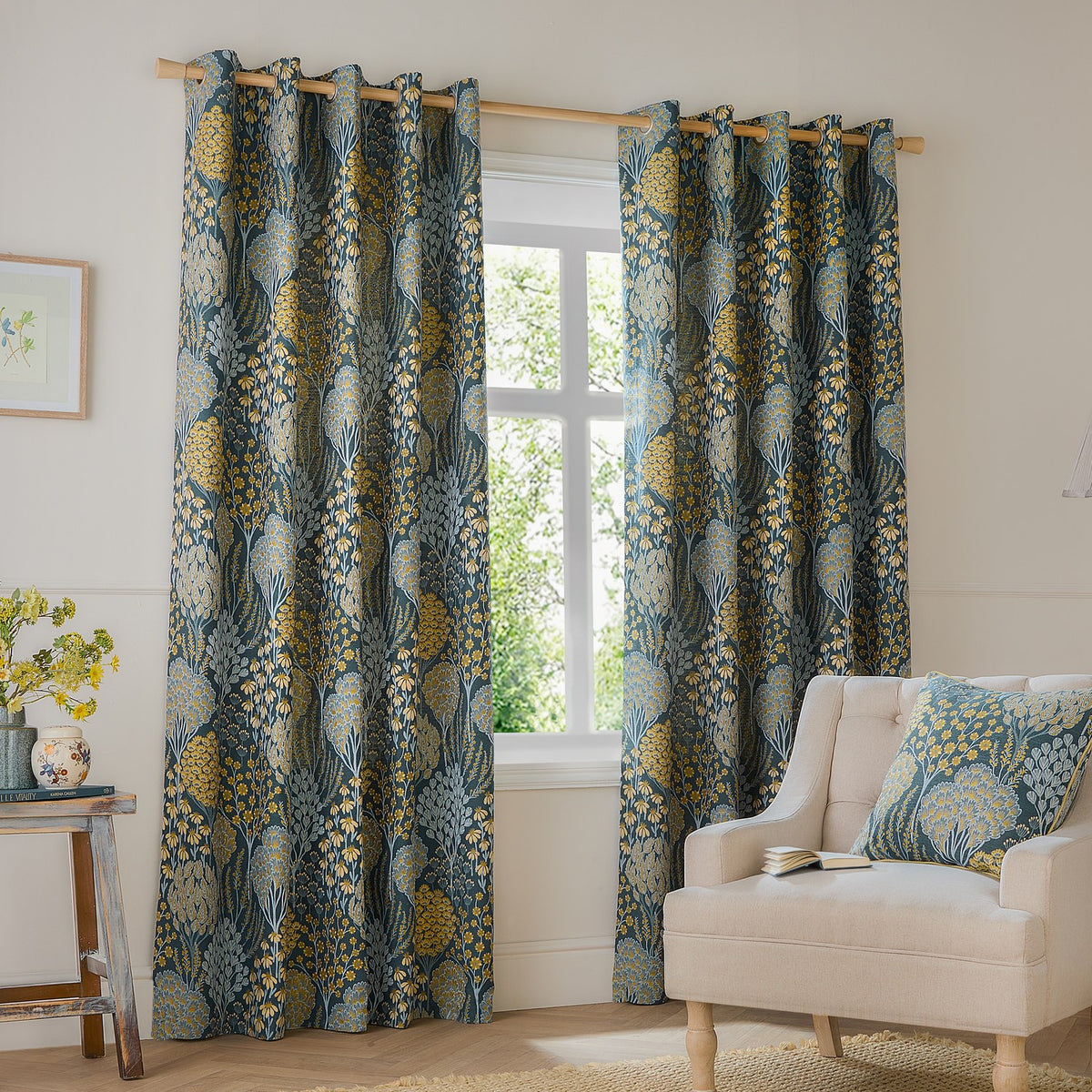 Ophelia Jacquard fully lined eyelet curtains in blue with saffron floral pattern, shown on a wooden pole in a living room beside an armchair.