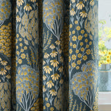 Ophelia Jacquard Fully Lined Eyelet Curtains in Blue/Saffron, shown draped in folds with a woven floral pattern of daisies and stylised trees in yellow, grey and blue on a teal ground.